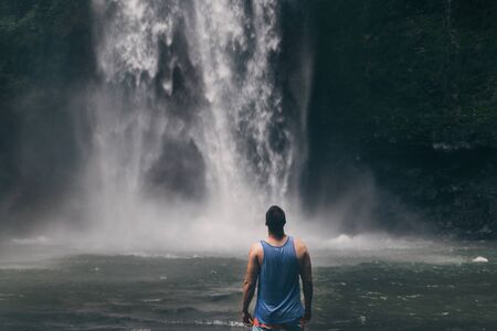 Young man standing in front of powerful Nungnung waterfall on Baliの写真素材