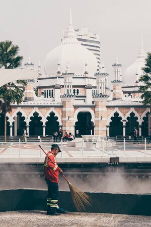 KUALA LUMPUR, MALAYSIA - JULY, 2019: Famous Masjid Jamek mosque in Kuala Lumpur and old janitor cleaning the streetのeditorial素材