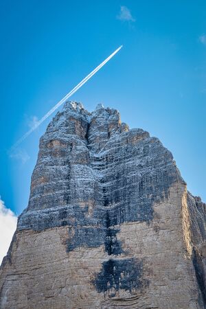 Dolomite rocky mountain covered with snow and flying plane in blue sky, Tre Cime di Lavaredo, Italy