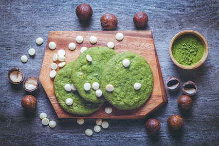 Matcha cookies with macadamia nuts and white chocolate chips on a dark wooden tableの写真素材