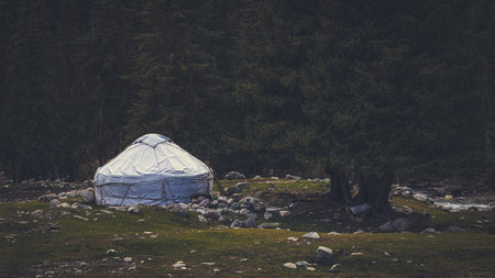 Traditional yurt house surrounded by beautiful coniferous forest and mountains in autumn, Kyrgyzstanの写真素材