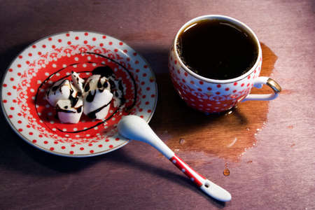 ceramic Cup polka dot spilled around coffee/tea spoon and a little bowl of ice cream watered with chocolate on wooden backgroundの写真素材