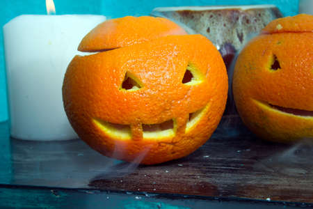 oranges with carved faces with white candles and a clay pot on a blue background with the autumn Halloween themeの写真素材