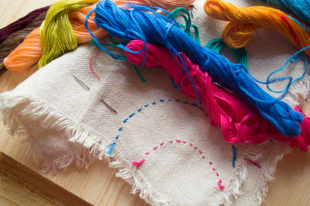 embroidery floss and cotton fabric with embroidery on wooden background. handmade concept. textile...