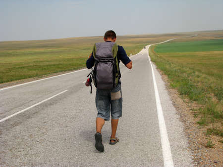 young man traveler with backpack is on the road in the upland steppe area in a summer Sunny day