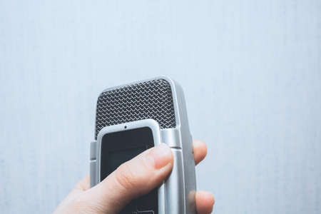 Hand holding microphone/voice recorder on a white background in retro colorsの写真素材