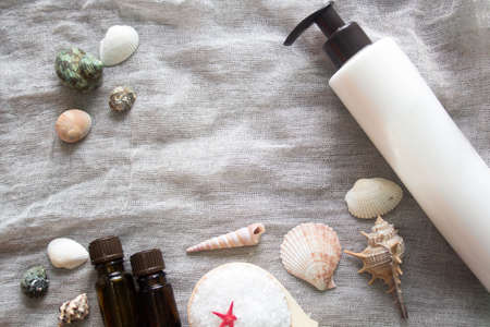 Shell, aromatherapy oil, bottle of body cream and a jar of sea salt on a grey cloth background. Spa...
