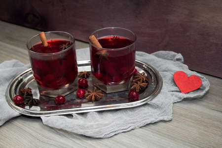 two glasses of mulled wine with cherries, cinnamon and star anise for lovers on silver vintage tray with red heart. concept for a romantic anniversary, Valentine's dayの写真素材