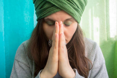 young beautiful woman in turban with closed eyes holding hands in the sign of Namasteの写真素材