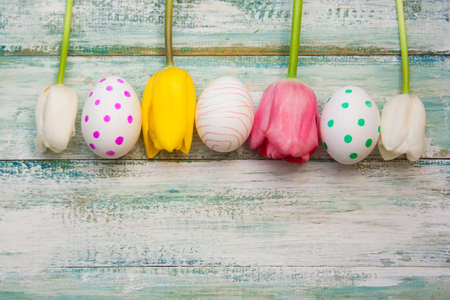tulips and polka dot eggs  on a vintage shabby light background, top view, empty copyspace.