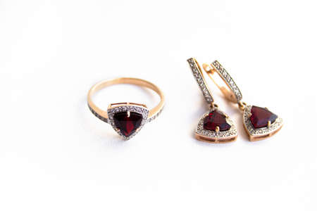 Gold ring and earrings with a red precious stone and small diamonds on a white background.の写真素材