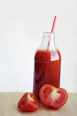 Freshly squeezed tomato juice in a bottle and tomato slices on a wooden table opposite the white wallの写真素材