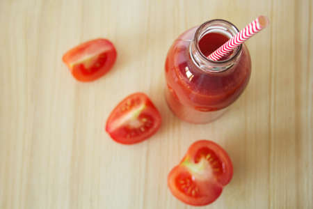 Freshly squeezed tomato juice in a bottle and tomato slices on a wooden table, top view.の写真素材