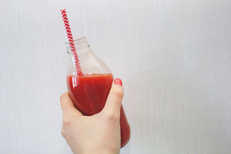 female hand holds a freshly squeezed tomato juice in a bottleの写真素材