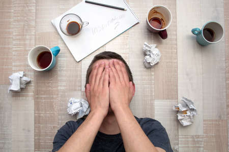 desperate man in search of inspiration, covered his face with his hands and lying on the floorの写真素材