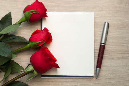 three roses, a pen and a blank piece of paper on the tableの写真素材