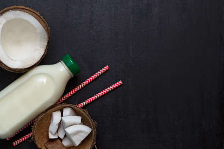 top view bottle of fresh raw vegan coconut milk and coconut on black background with place for textの写真素材