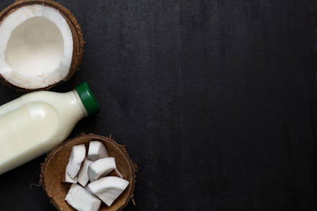 top view bottle of fresh raw vegan coconut milk and coconut on black background with place for textの写真素材