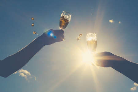 Hands of man and woman clink wineglasses of sparkling white wine on  sky and sun. retro tonedの写真素材