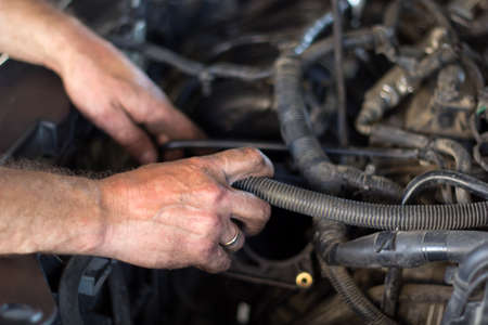 Auto mechanic working under the hood of an old car engine.