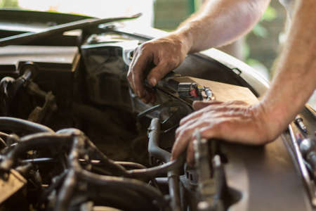 Auto mechanic working under the hood of an old car engine.の写真素材