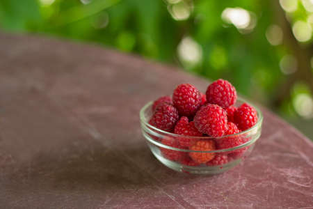 fresh raspberries in a glass bowl on a table in a gazeboの写真素材