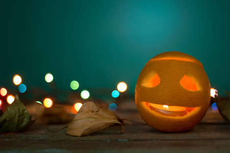 candle holder for Halloween made from orange carved with scary face among the autumn leaves on a wooden table.の写真素材