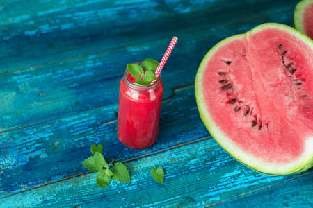 resh watermelon juice with mint in a jar with a straw on a blue wooden tableの写真素材