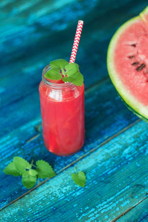 resh watermelon juice with mint in a jar with a straw on a blue wooden tableの写真素材