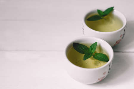 two mugs of green tea with mint on a white tableの写真素材