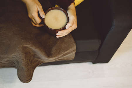 girl with a warming drink in hand lying on the sofa with a blanket