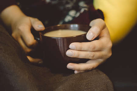 girl with a warming drink in hand lying on the sofa with a blanketの写真素材