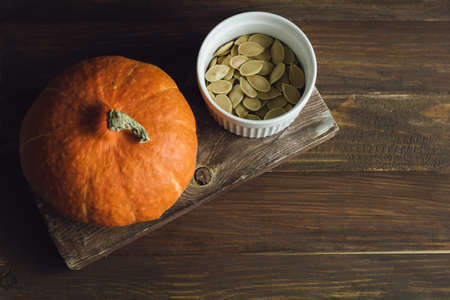 bowl with  dried pumpkin seeds and a little pumpkin on a brown table, top viewの写真素材