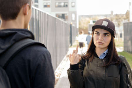 a young girl in the cap shows the middle finger (fuck you sign) with my boyfriend( man's back)の写真素材