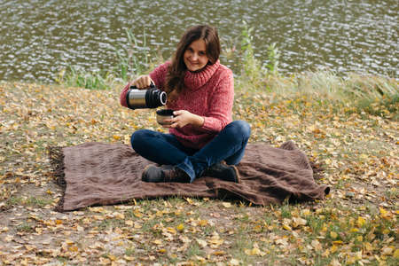 girl on picnic in the  park near the river and pours tea from a thermosの写真素材
