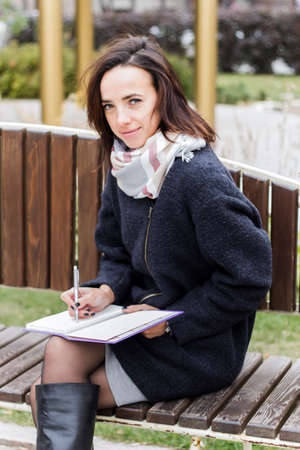 young girl sitting on a bench in a park and working with a daily planner.の写真素材