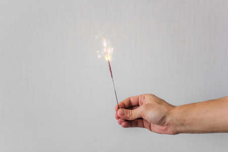 male hand holding a sparkler in front of the white wallの写真素材