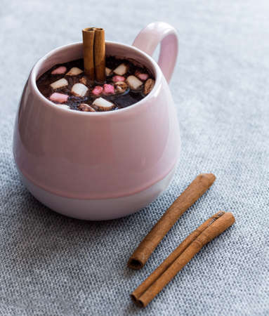 hot chocolate  pink ceramic mug marshmallows and cinnamon sticks gray knitted background