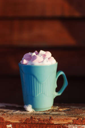 Blue mug of drink with whipped cream and marshmallows on wooden background with snowの写真素材