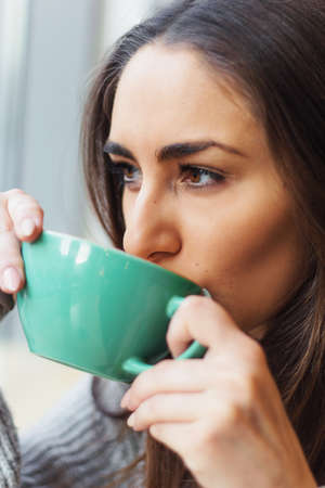 Close up portrait of beautiful brunette girl drinking coffee from a blue mug in the coffee shop