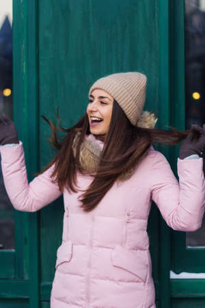 portrait of happy young smiling woman in a pink jacket and a cap opposite the green wallの写真素材