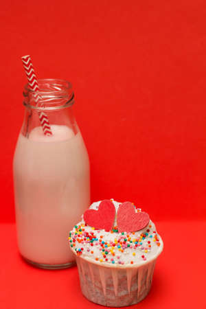 pink strawberry milkshake in a bottle with a cocktail straw and cute cupcake on red  backgroundの写真素材