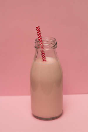 Pink strawberry milk shake in a bottle with a cocktail straw on a pink backgroundの写真素材