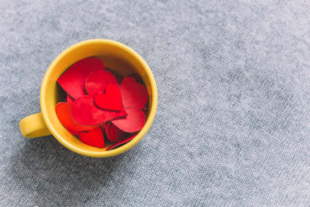 top view yellow cup full of paper red hearts on grey knitted background copy spaceの写真素材