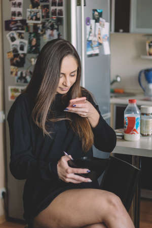 beautiful young brunette girl in a black sweatshirt using smartphone  and eating  cerealの写真素材