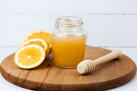 Jar of honey and lemon slices on a wooden board light backgroundの写真素材