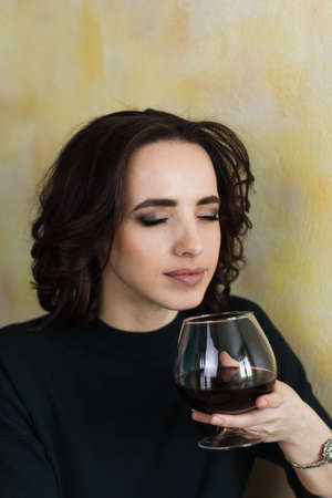 beautiful woman with closed eyes holds a glass of red wine and inhales its aromaの写真素材