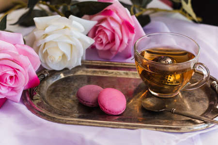 pink macaroons, hot tea on silver vintage tray blurred roses backgroundの写真素材