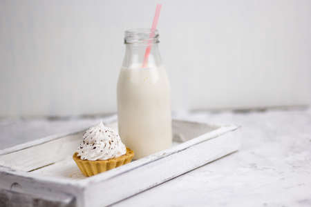 cupake with vanilla cream decorated with chocolate chips and milk bottle on a wooden trayの写真素材