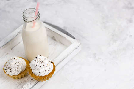 cupake with vanilla cream decorated with chocolate chips and milk bottle on a wooden tray copy space concrete backgroundの写真素材